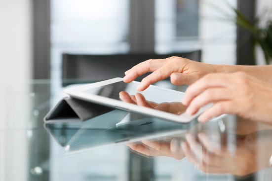 Hände bedienen ein Tablet auf einem Glastisch